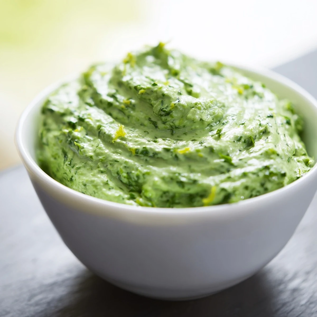 A bowl of cool Green Goddess Dip, speckled with fresh herbs, ready for a party.