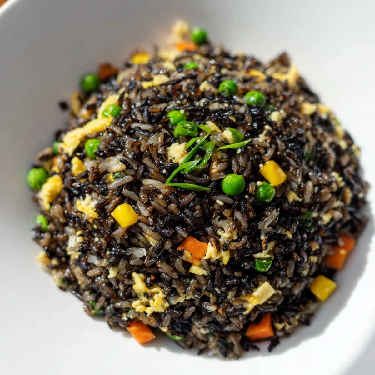 A steaming bowl of Black Garlic Fried Rice, garnished with fresh scallion greens and served alongside tangy kimchi.  