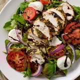 A beautiful Caprese Chicken Salad displays grilled chicken atop fresh ingredients and a balsamic drizzle.