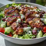 Fresh and vibrant Greek salad bowl featuring juicy grilled chicken, crisp lettuce, and tangy feta.  