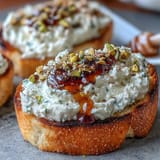 Elegant appetizer featuring golden baguette slices spread with fluffy ricotta, sweet honey, and nutty pistachios.