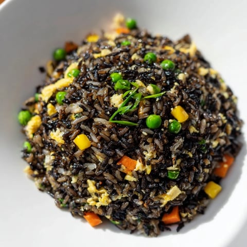 A steaming bowl of Black Garlic Fried Rice, garnished with fresh scallion greens and served alongside tangy kimchi.  