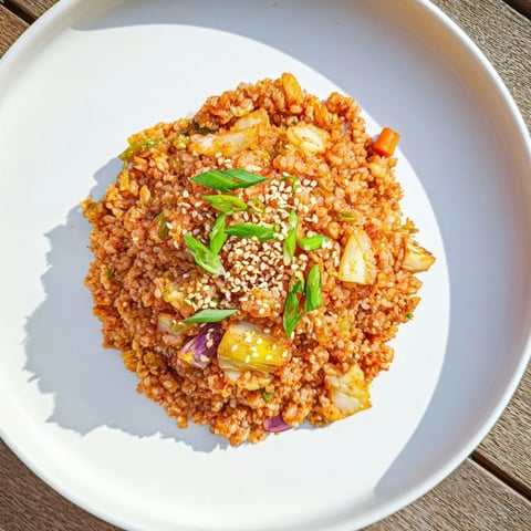 A vibrant bowl of Kimchi Fried Rice topped with a sunny-side-up fried egg and sesame seeds, steaming on a wooden table.