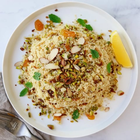 A bowl of fluffy Couscous Pilaf Spiced with cumin, cinnamon, and turmeric, dotted with golden apricots, raisins, and crunchy toasted nuts.