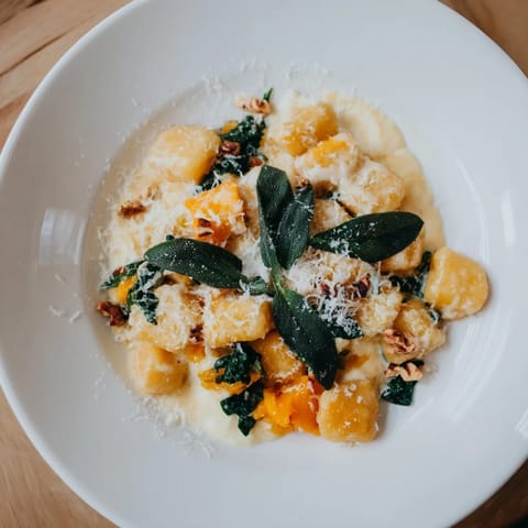 Close-up of golden-hued One-Pot Creamy Pumpkin Sage Gnocchi, thick sauce enveloping fluffy gnocchi.