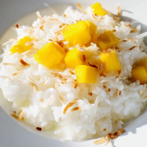 A close-up of tropical Coconut Rice Sweet topped with toasted coconut flakes and vibrant mango, ready to be served.
