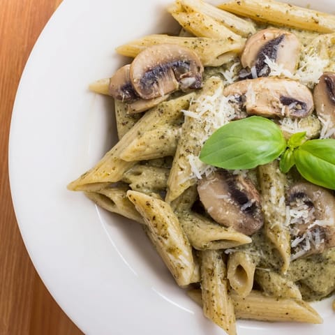 Hearty mushroom pesto pasta served in a white bowl, topped with grated Parmesan and vibrant green basil.  
