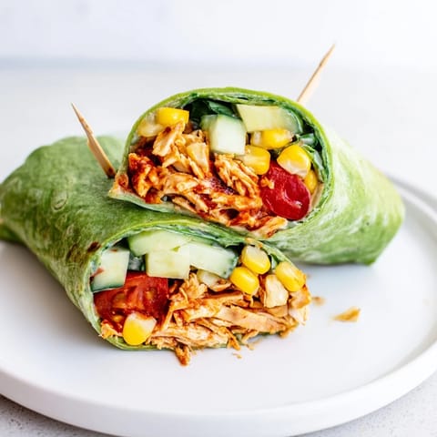 A hearty BBQ Chicken Salad Wrap sliced in half, revealing colorful layers of veggies and creamy dressing.