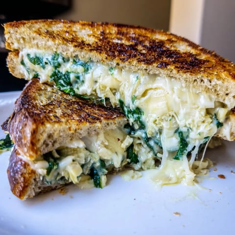 Artichoke Spinach Grilled Cheese sandwich on a plate, paired with a bowl of tomato soup for a cozy lunch.