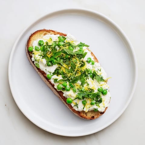 Bright lemon zest and fresh mint top this vibrant Pea & Mint Ricotta Toast, served on a rustic plate.  