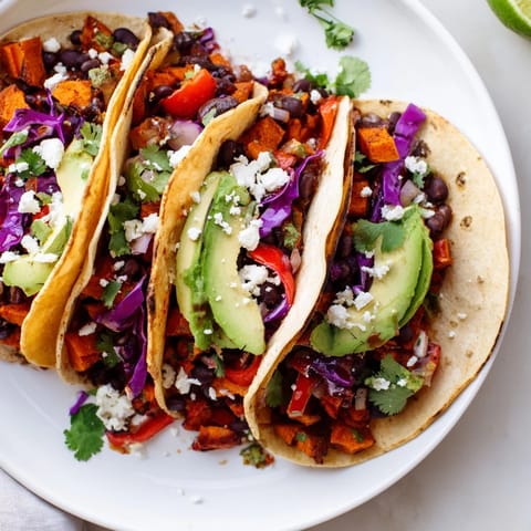 Savory Black Bean and Sweet Potato Tacos featuring vibrant roasted vegetables, seasoned with cumin and smoked paprika, then piled high with tangy vegan feta and a drizzle of cool sour cream.