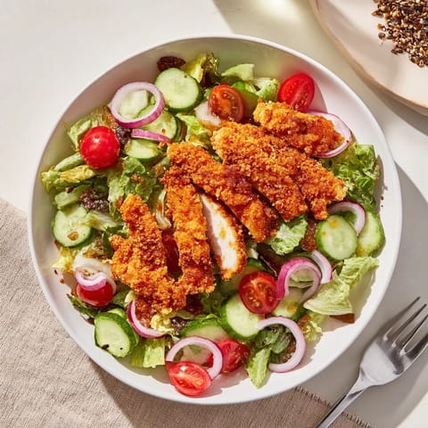 Golden crispy chicken sits atop a vibrant bed of romaine, cucumber, and tomatoes, finished with a sweet heat drizzle.