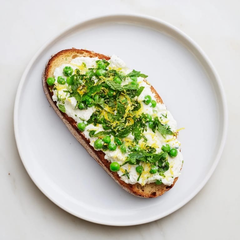 Bright lemon zest and fresh mint top this vibrant Pea & Mint Ricotta Toast, served on a rustic plate.  