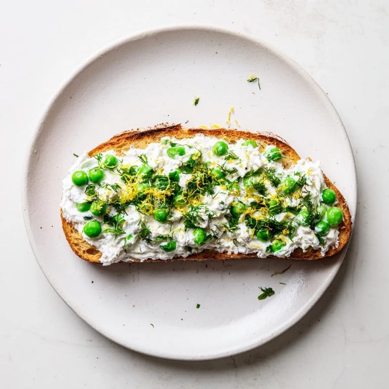 A slice of warm Pea & Mint Ricotta Toast garnished with mint, ready for a sunny brunch spread.