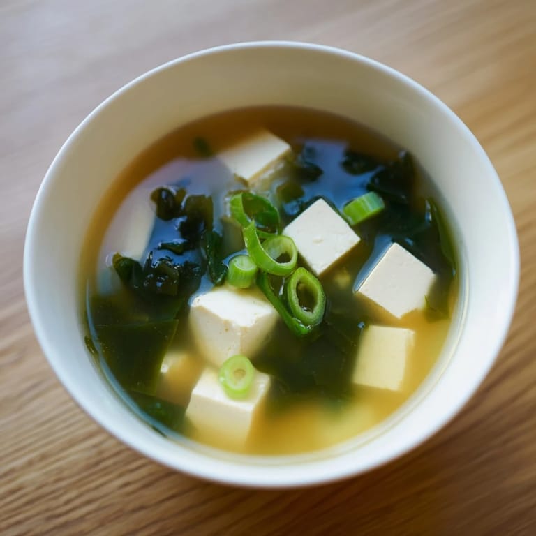 Miso soup with tofu in a traditional ceramic bowl, highlighting the delicate texture of silken tofu cubes and nutrient-rich seaweed in a comforting broth.