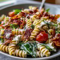 A colorful BLT pasta salad with bacon, avocado, cherry tomatoes, and crisp lettuce in a creamy dressing.